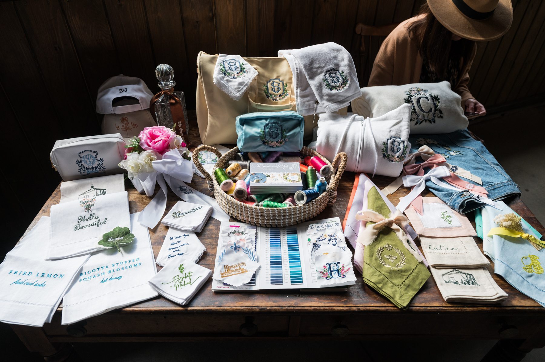 A table full of a variety of embroidered monogram examples like handkerchiefs, bags, napkins and ribbons made by The Handkerchief Shop.